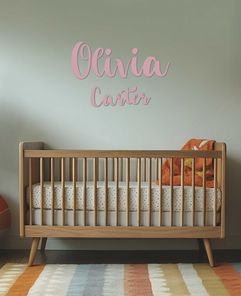 A nursery with a light wall featuring pink script &quot;Olivia Carter&quot; decals above a mid-century modern wooden crib.