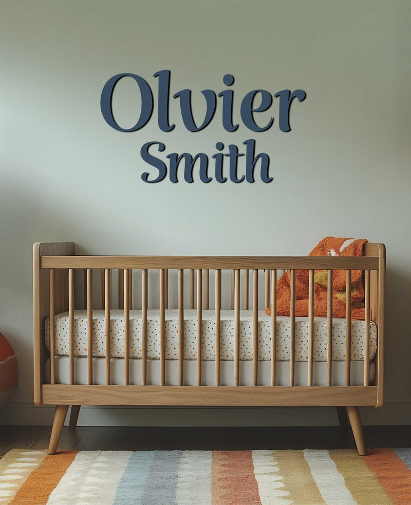 A nursery showcasing &quot;Oliver Smith&quot; in navy blue script above a wooden crib.